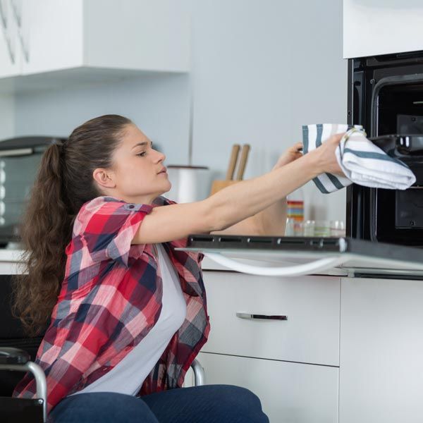 Woman reaching up to microwave oven from wheelchair